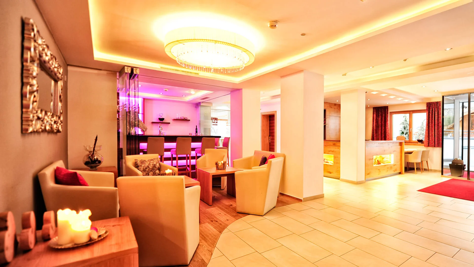 Impressionen | Hotel Alpenland in Ischgl Helle Hotellobby mit Sitzgruppen, Bar, Kamin und großem Kronleuchter