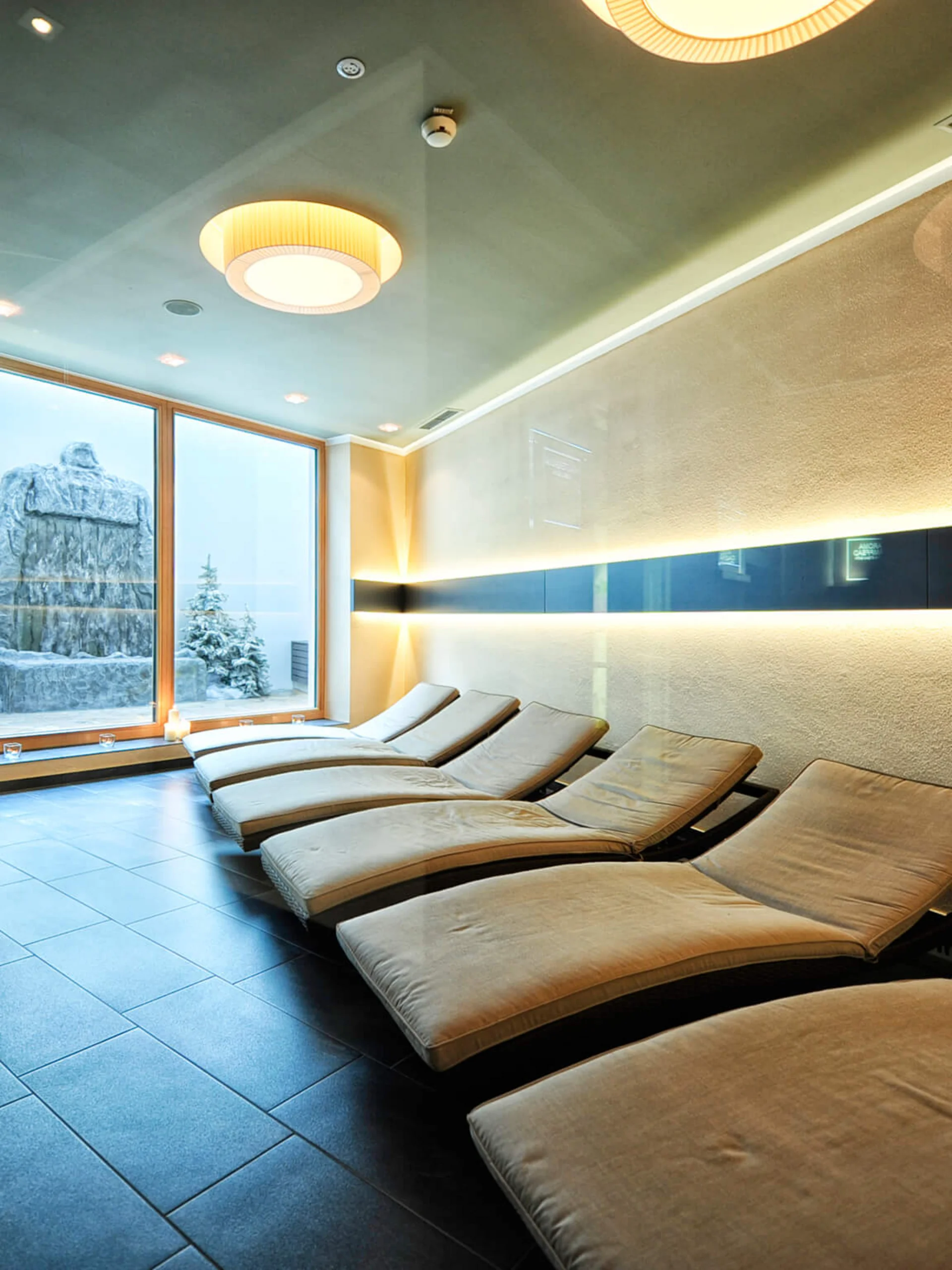 Impressionen | Hotel Alpenland in Ischgl Ruheraum mit Liegestühlen und verschneiter Berglandschaft vor dem Fenster