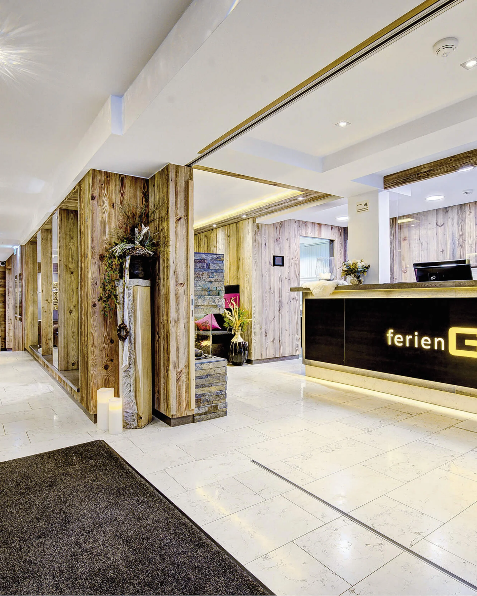 Ferienglück and Alpenland | Your stylish hotels in Ischgl Bright hotel reception with wood paneling and illuminated FerienGlück sign