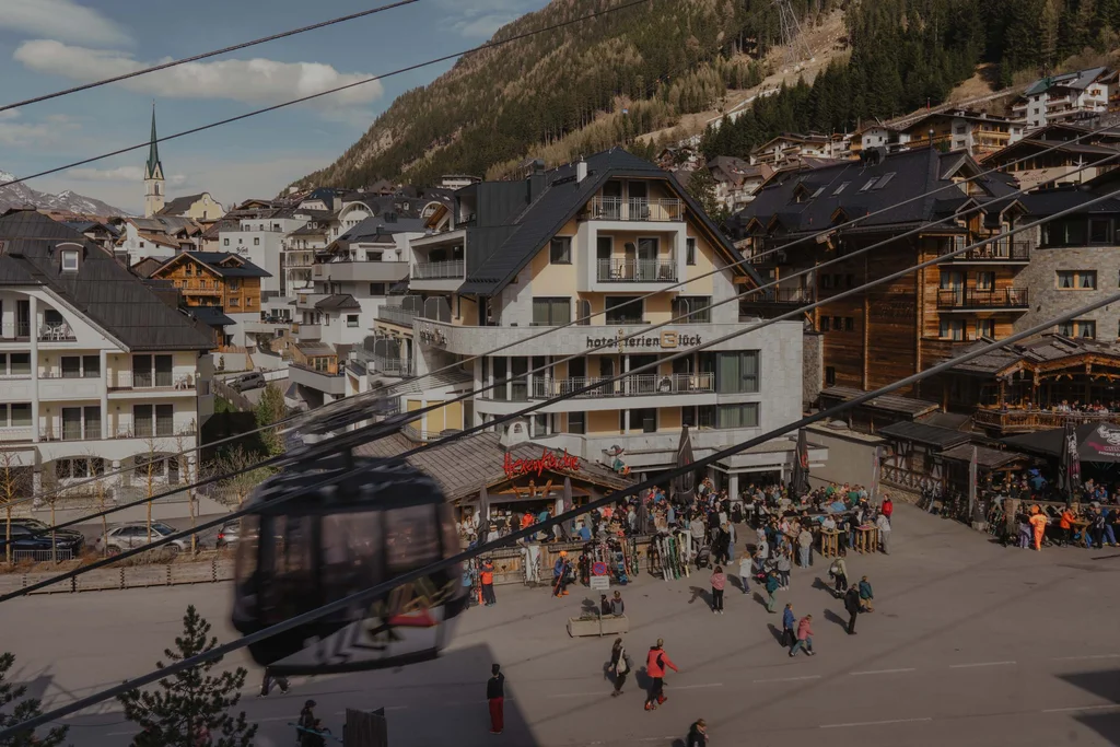 Ferienglück and Alpenland | Your stylish hotels in Ischgl Mountain village with cable car cabin, alpine backdrop, hotels and many people