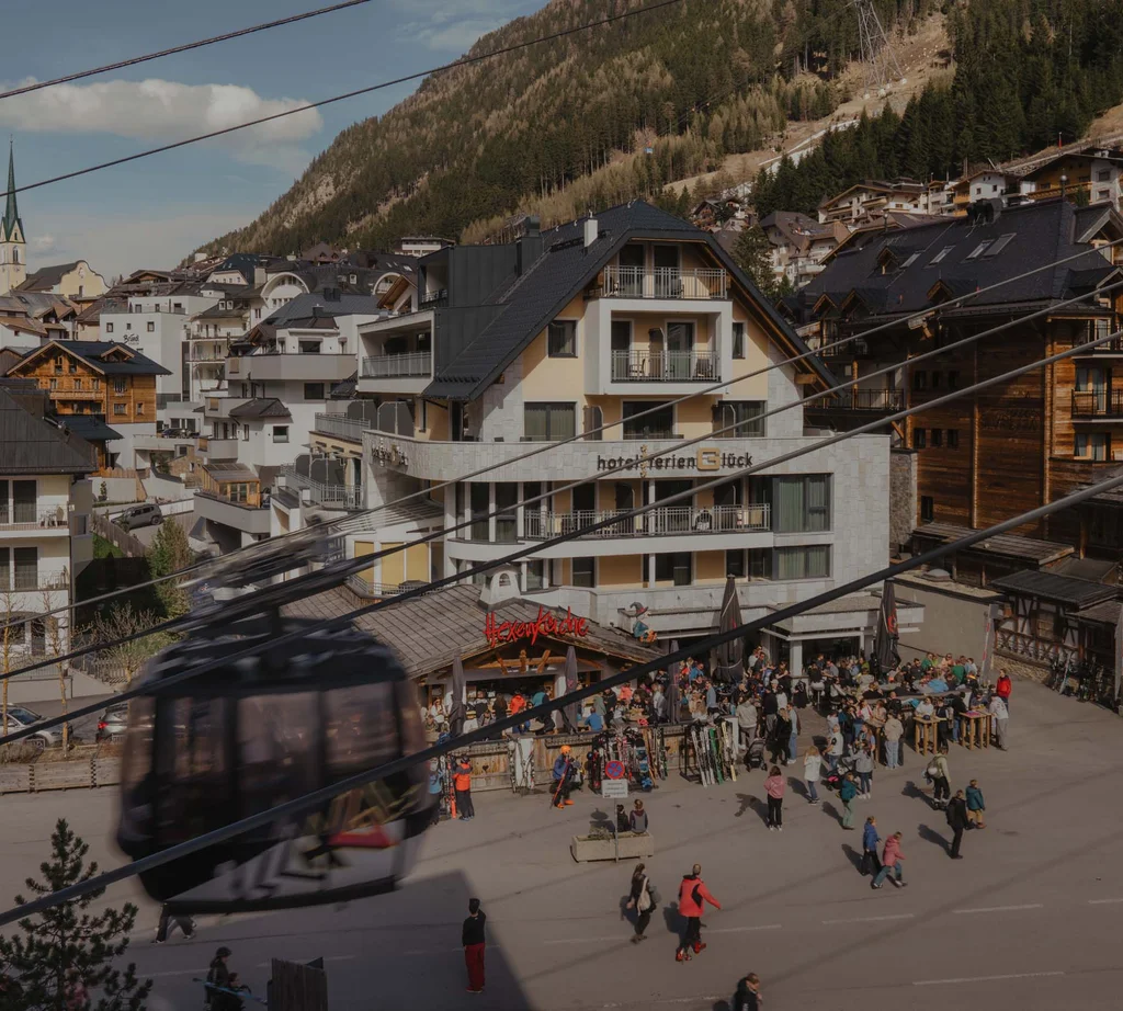 Ferienglück and Alpenland | Your stylish hotels in Ischgl Mountain village with cable car cabin, alpine backdrop, hotels and many people