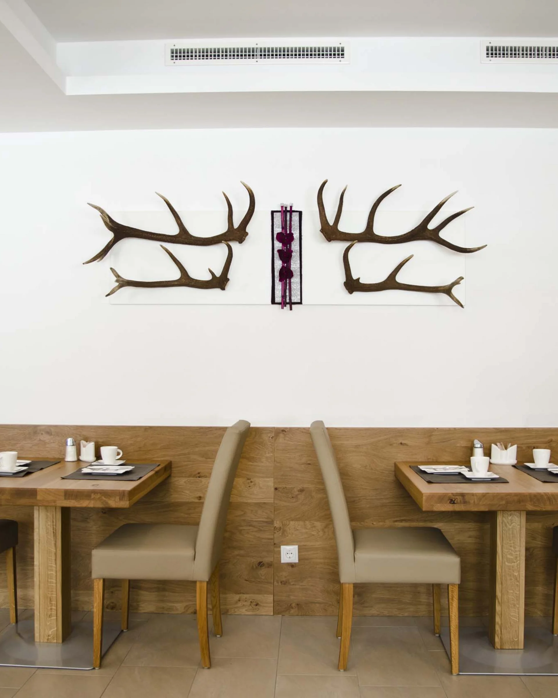 Impressionen | Hotel Alpenland in Ischgl Hotelrestaurant mit gedeckten Holztischen und Hirschgeweih-Wanddekoration