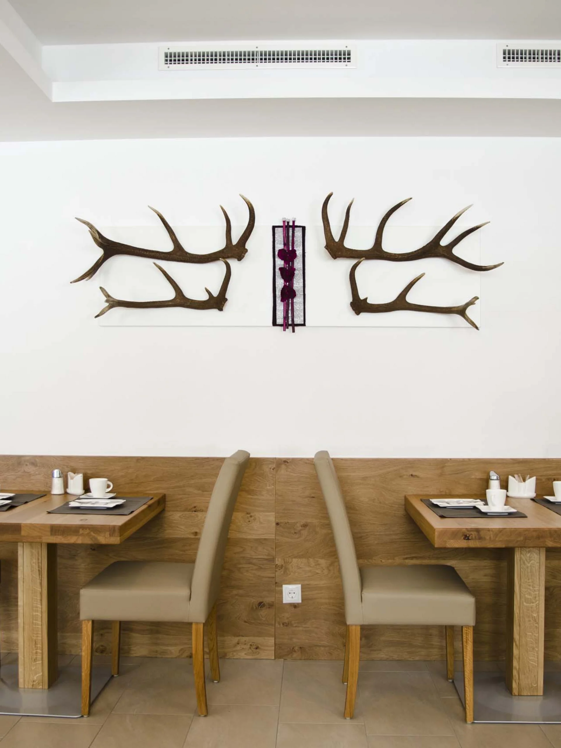 Impressionen | Hotel Alpenland in Ischgl Hotelrestaurant mit gedeckten Holztischen und Hirschgeweih-Wanddekoration