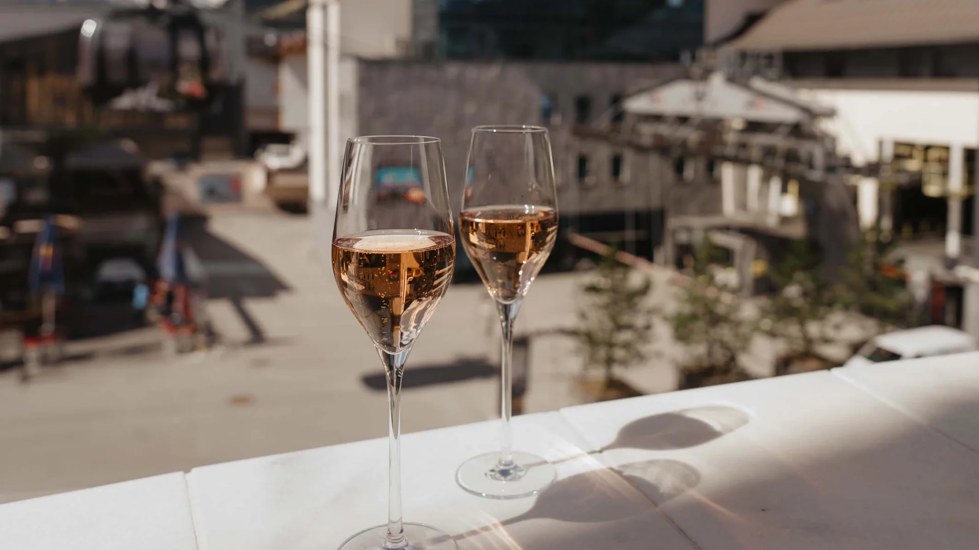 Ferienglück and Alpenland | Your stylish hotels in Ischgl Two filled wine glasses on a terrace overlooking a mountain village