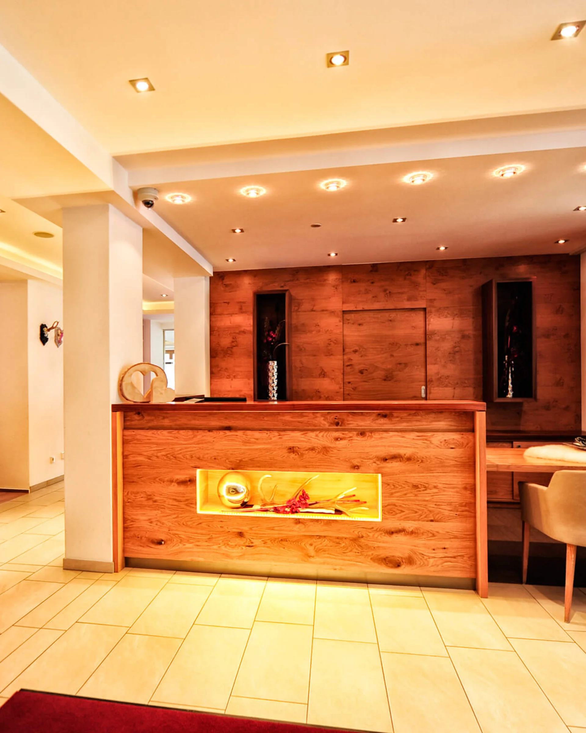 Impressionen | Hotel Alpenland in Ischgl Hotelrezeption mit Holztresen, Sitzbereich und beleuchtetem Barbereich