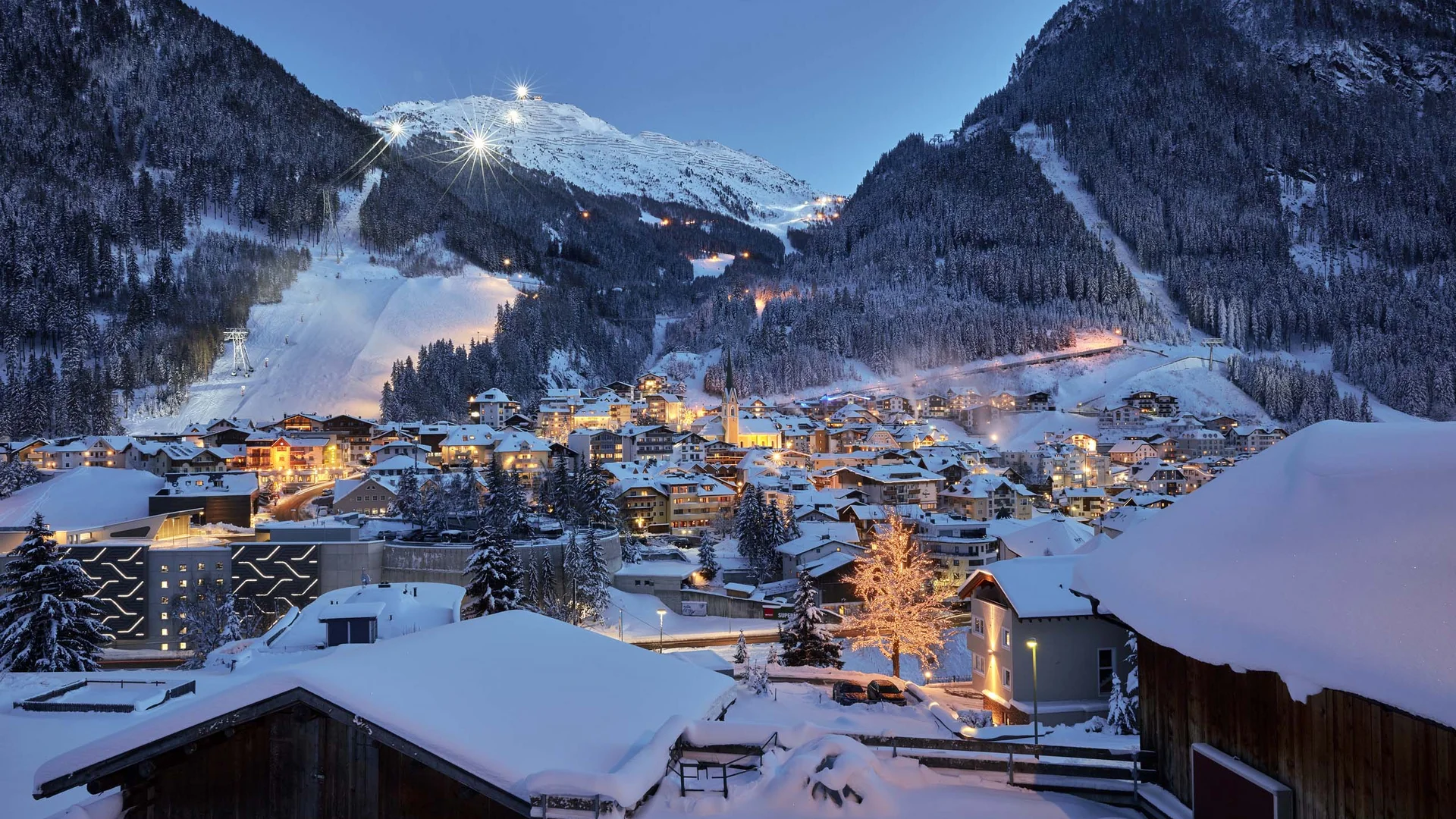 Impressionen | Hotel Alpenland in Ischgl Verschneites Bergdorf mit beleuchteten Häusern und Skipisten bei Dämmerung