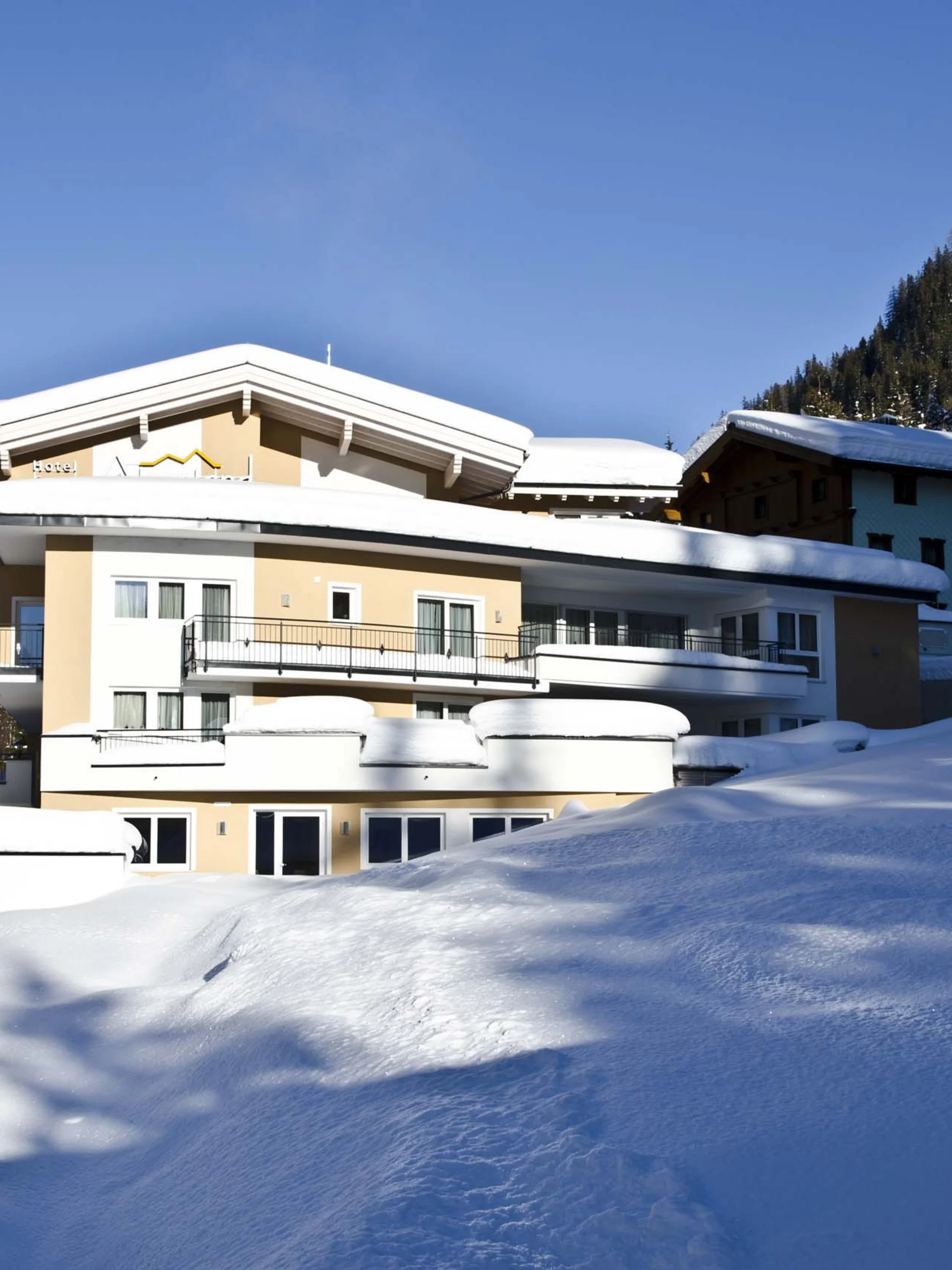 Impressionen | Hotel Alpenland in Ischgl Verschneites Hotel in den Bergen bei strahlend blauem Himmel