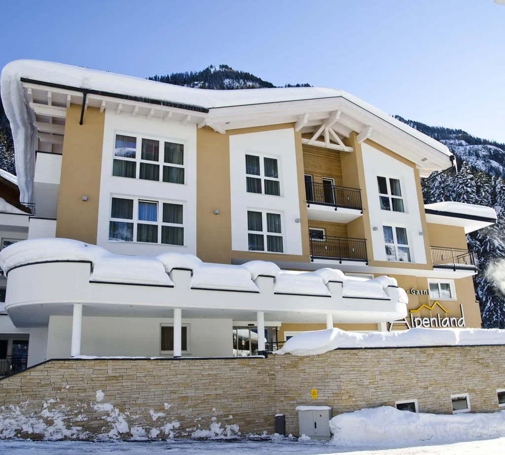 Ferienglück and Alpenland | Your stylish hotels in Ischgl Snow-covered Hotel Alpenland in front of forested mountains
