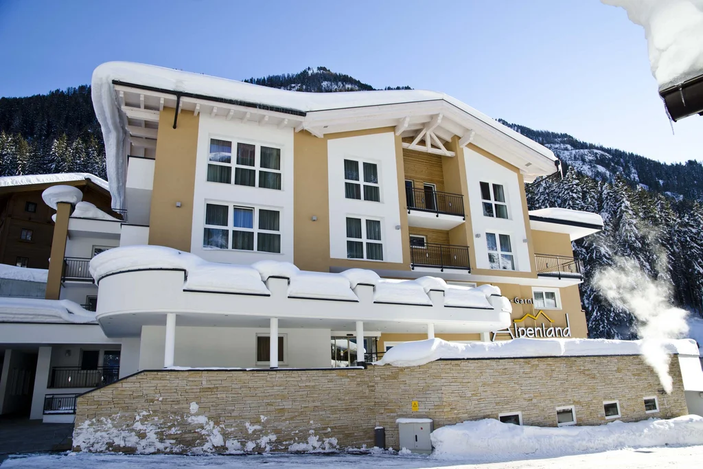 Ferienglück and Alpenland | Your stylish hotels in Ischgl Snow-covered Hotel Alpenland in front of forested mountains