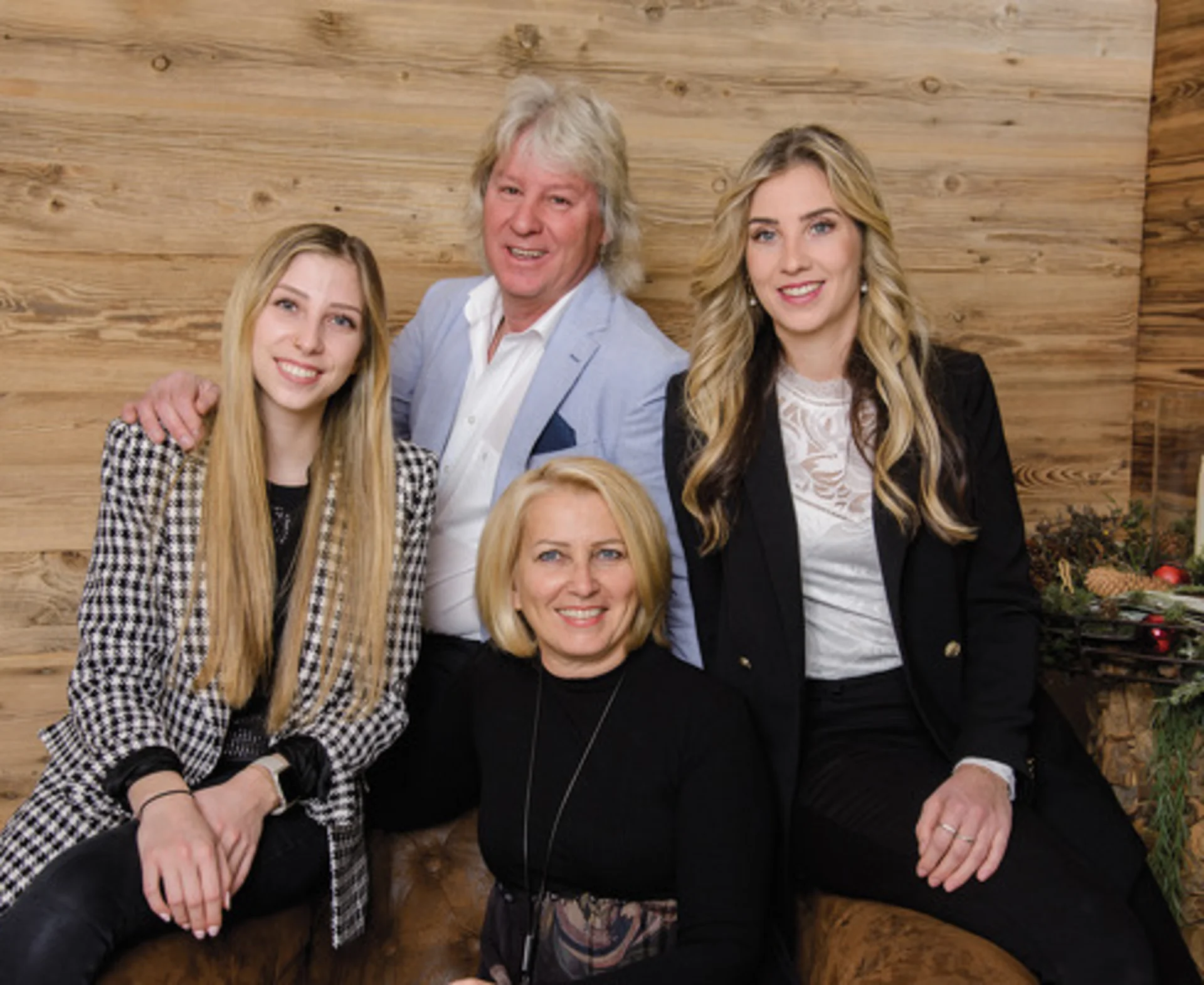 Ferienglück and Alpenland | Your stylish hotels in Ischgl Four people pose in front of a wooden wall beside Christmas decorations