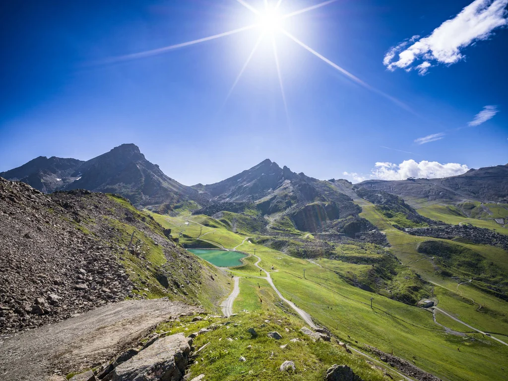 Ferienglück and Alpenland | Your stylish hotels in Ischgl Sunny mountain landscape with hiking trails, green slopes and a small alpine lake