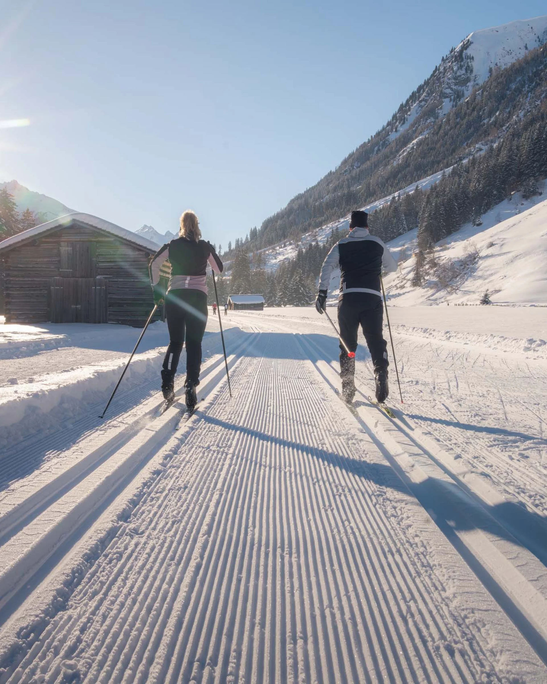 Impressionen | Hotel Alpenland in Ischgl Zwei Langläufer auf einer verschneiten Loipe vor alpiner Bergkulisse