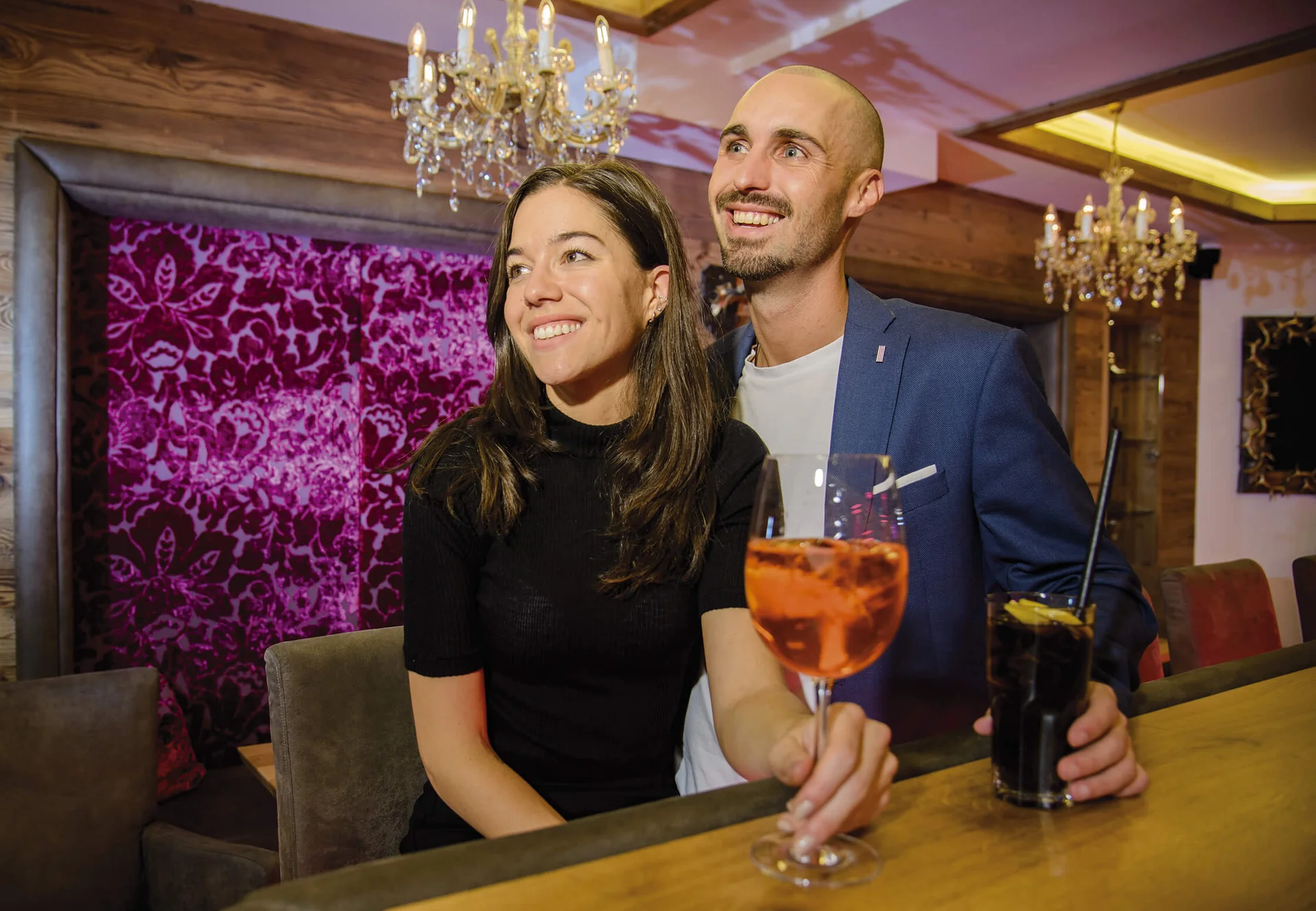 Ferienglück and Alpenland | Your stylish hotels in Ischgl Couple with cocktails in a stylish bar with chandeliers
