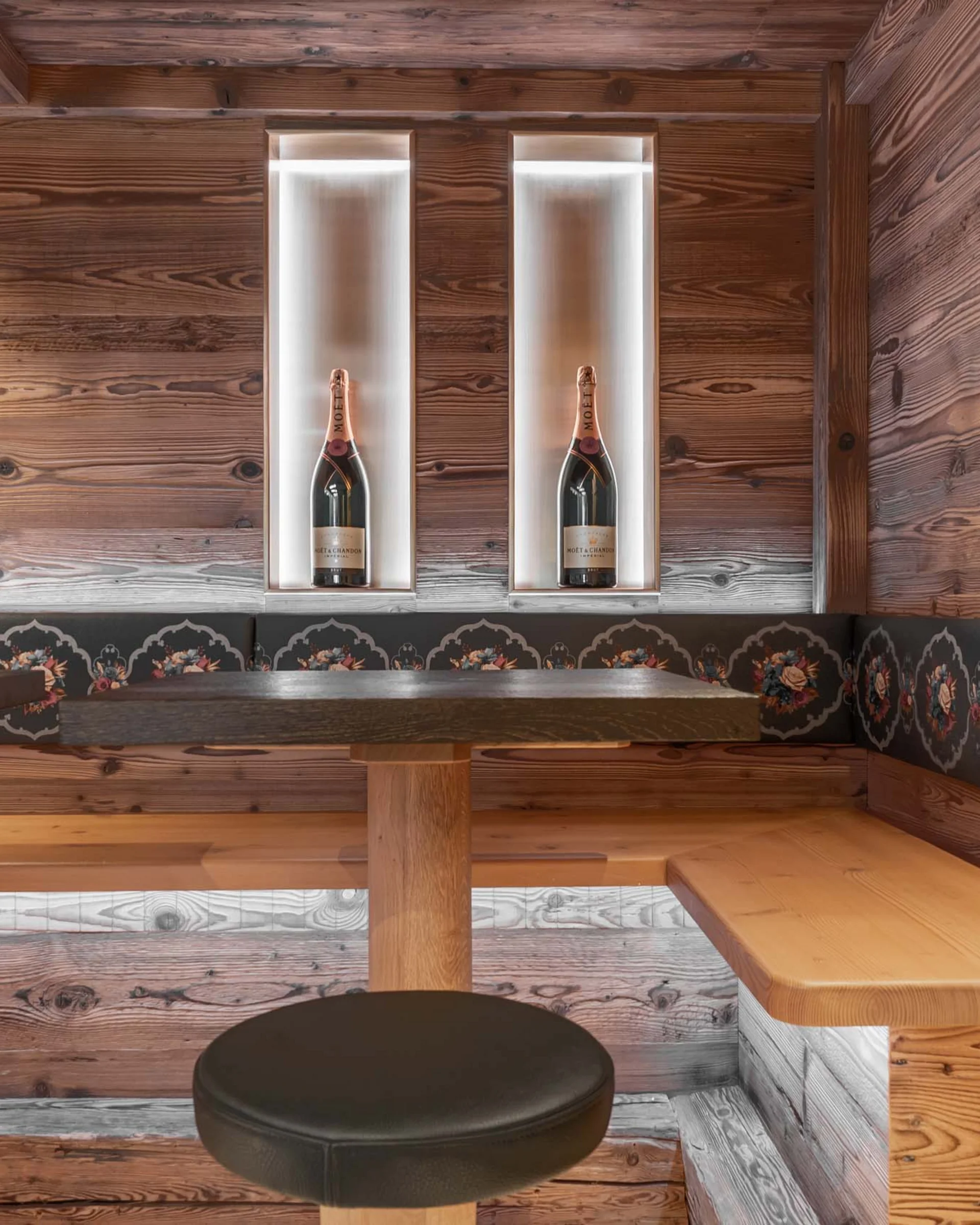 Ferienglück and Alpenland | Your stylish hotels in Ischgl Rustic wooden dining nook with floral bench, table and two bottles in wall niches