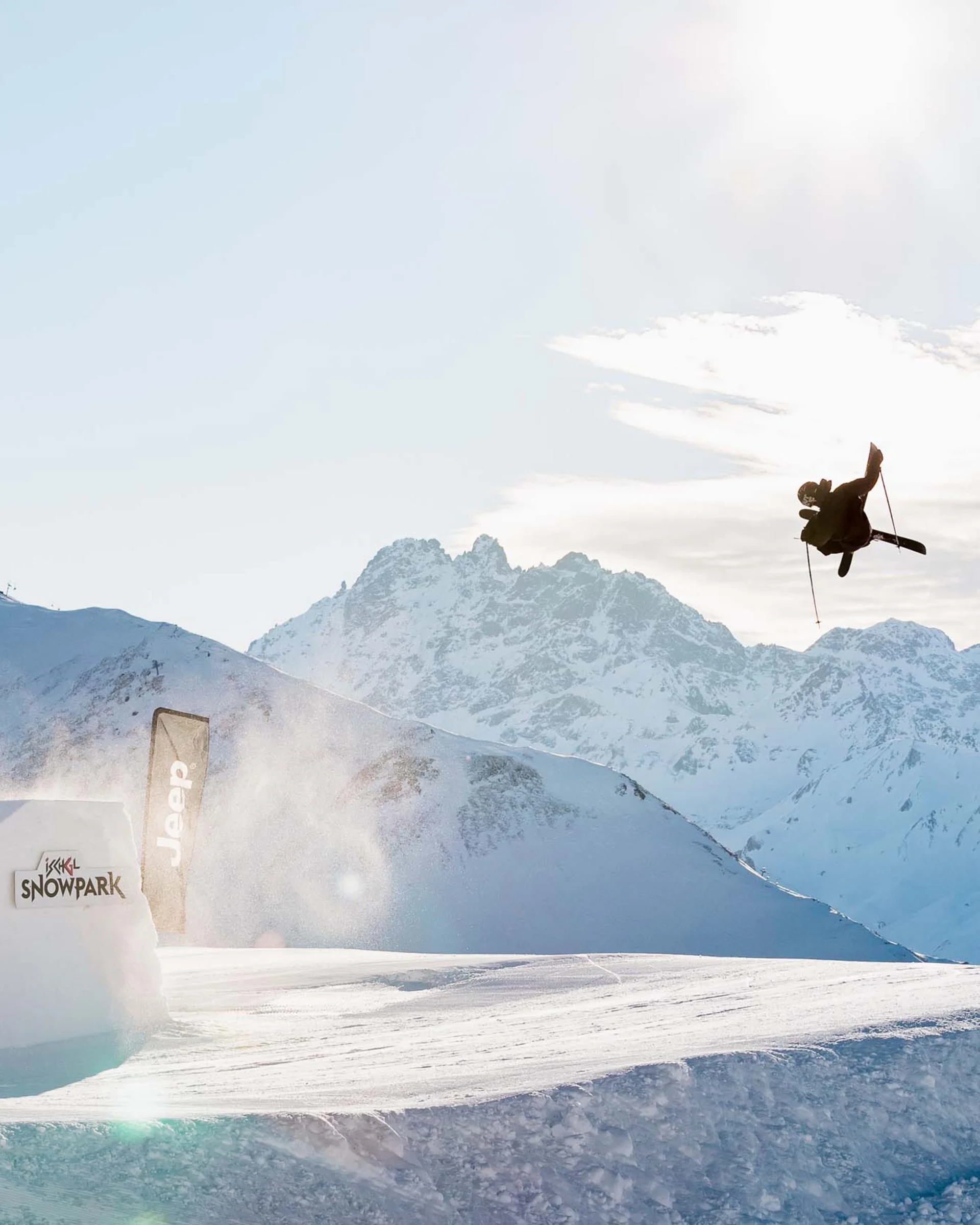 Impressionen | Hotel Alpenland in Ischgl Wintersportler springt über eine Schneeschanze vor verschneiten Bergen
