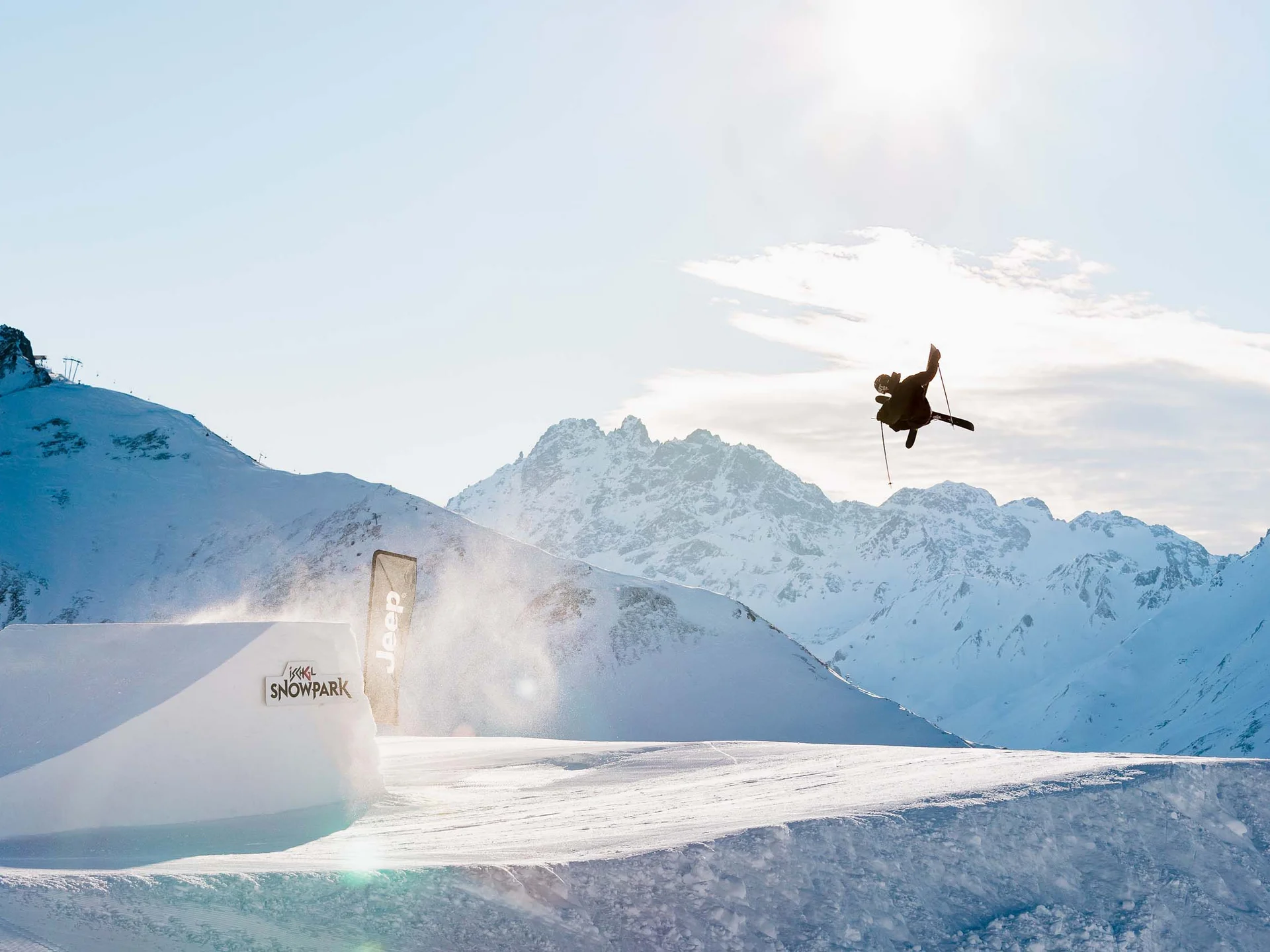 Impressionen | Hotel Alpenland in Ischgl Wintersportler springt über eine Schneeschanze vor verschneiten Bergen