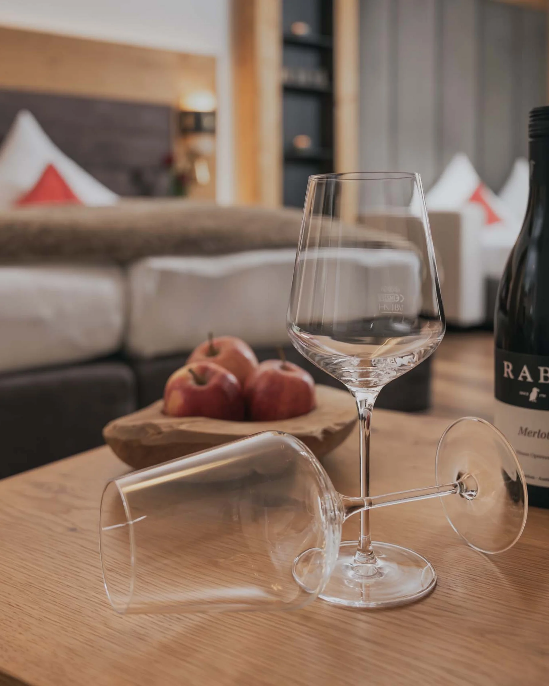 Ferienglück and Alpenland | Your stylish hotels in Ischgl Wine bottle, two wine glasses and apples on a wooden table in front of a sofa
