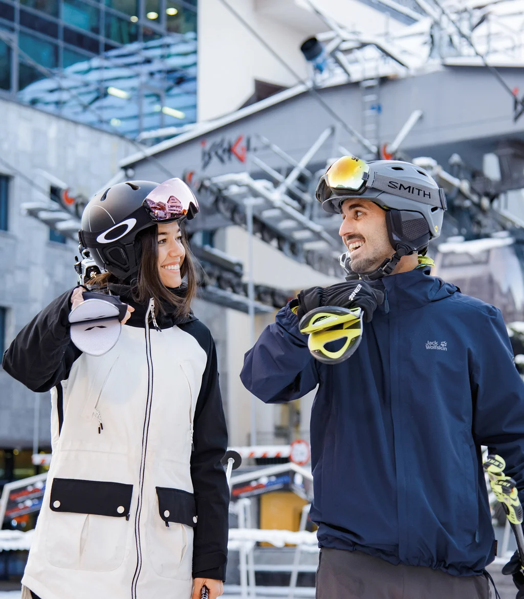 Ferienglück and Alpenland | Your stylish hotels in Ischgl Two winter sports enthusiasts wearing helmets in front of a snowy ski lift